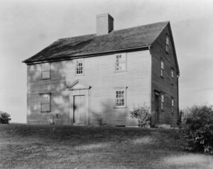 Black and white image of moderately sized two-story colonial house on grassy hill