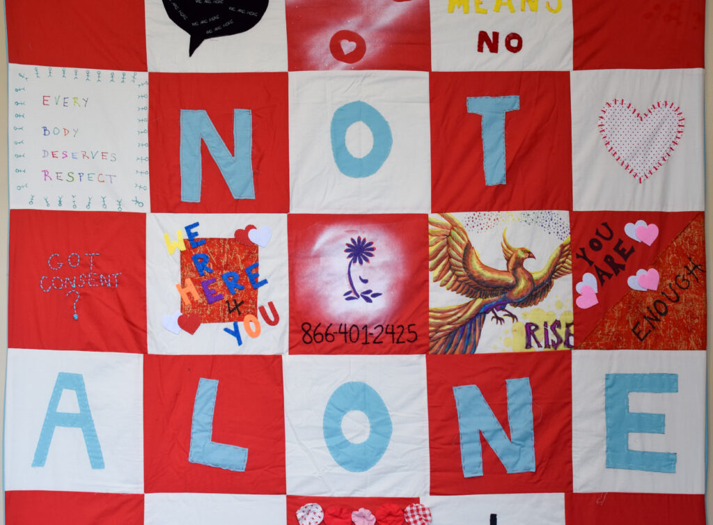 Red and white quilt with words "Not Alone" in blue letters